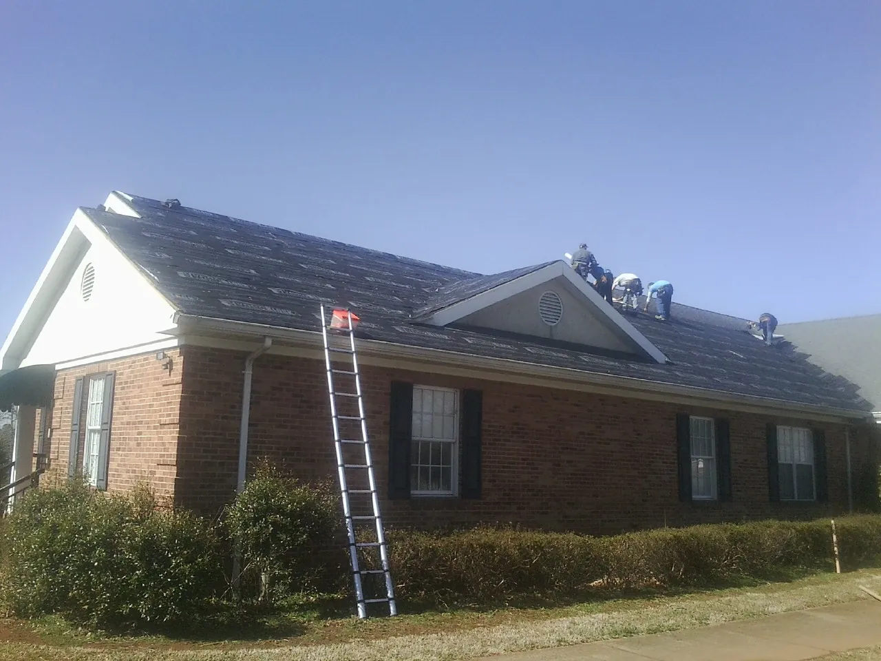 Crew tearing shingles off a brick ranch roof with a ladder set — Emergency Roof Repair work by our crew in Hancock